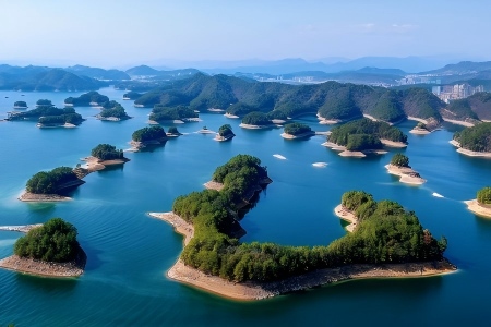 Bird’s-eye shot of countless forest-covered small islands scattered in clear blue water of Qiandao Lake, layered mountain backdrop under bright sky