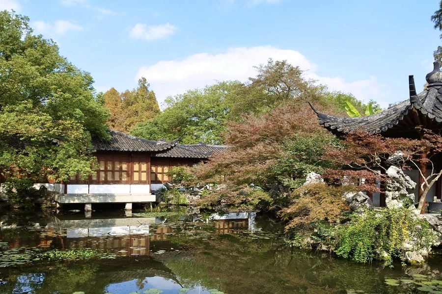 Traditional wooden waterside buildings, rockeries and maple trees reflected in quiet pond at Guo Zhuang Garden beside West Lake