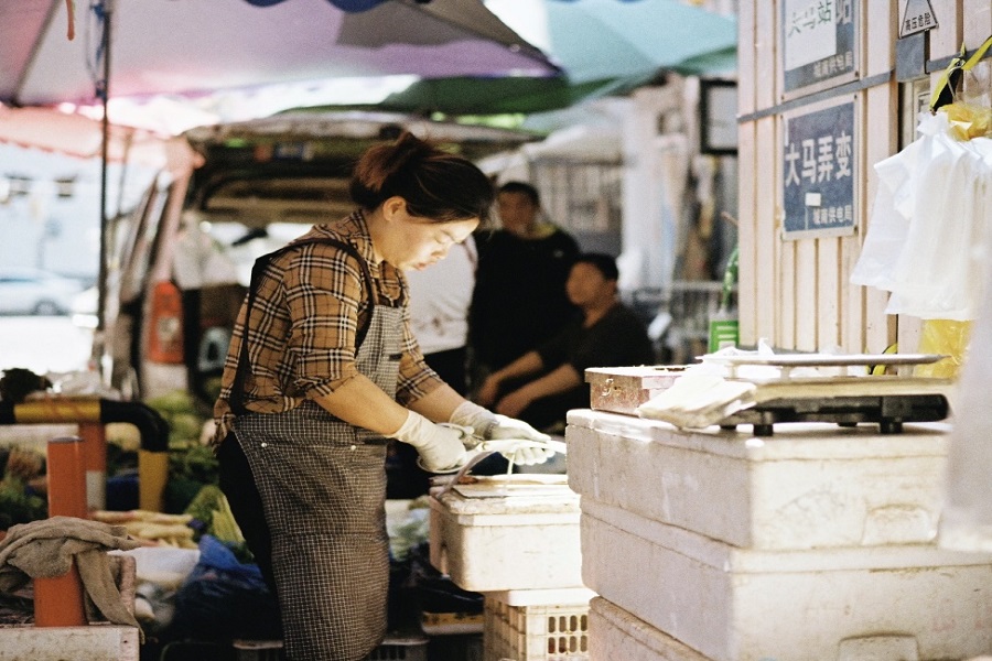 Local shopkeeper preparing fresh produce at bustling Damalong street market, Hangzhou daily life scene