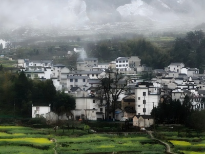 Foggy mountain village featuring classic Huizhou white-walled buildings surrounded by green terraced farmland