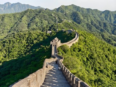 Mutianyu Great Wall with steep stone steps and watchtower, snaking over lush green forested hills under clear sky, iconic Beijing landmark